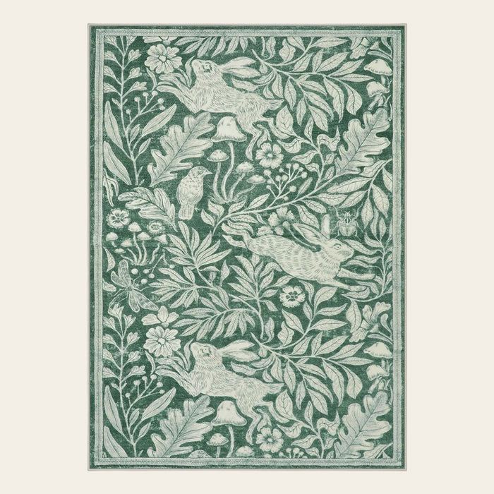 Covaba vintage woodcut forest and rabbit area rug in fern green, shown flat on a plain ivory backdrop