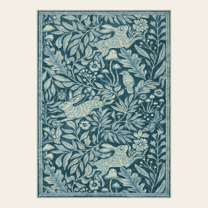 Covaba vintage woodcut forest and rabbit area rug in stormy blue, shown flat on a plain ivory backdrop