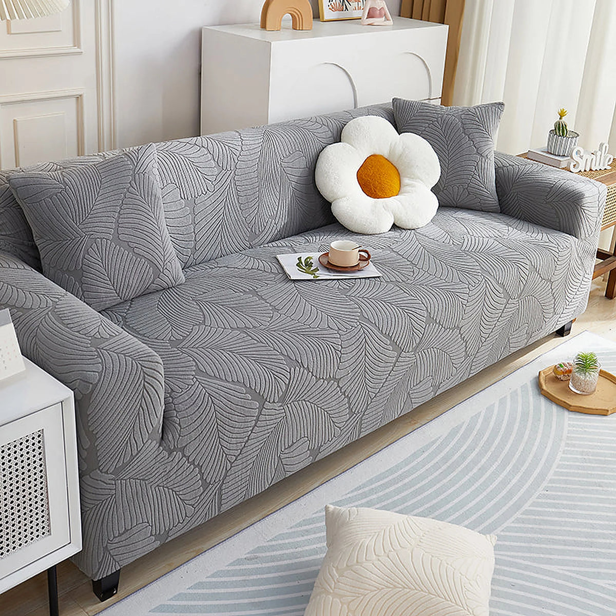 Stone Grey Palm Relief sofa cover draped over a three-seater sofa in a bright living room, view 4
