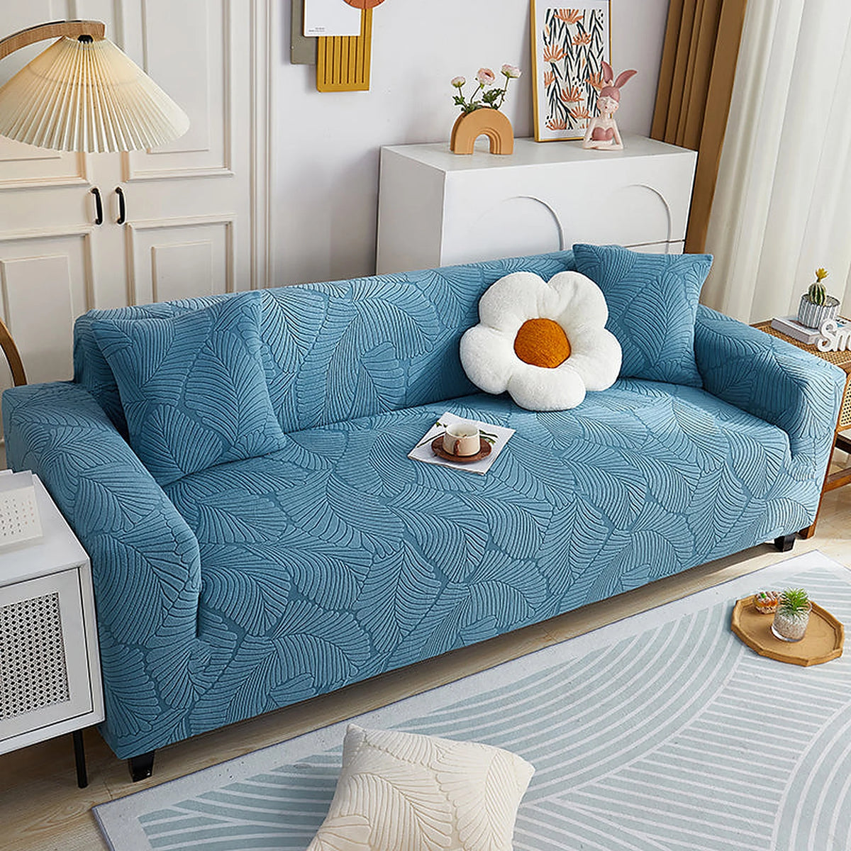 Stormy Blue Palm Relief sofa cover draped over a three-seater sofa in a bright living room