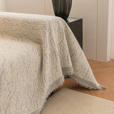 Stone Grey Wave Quilted sofa throw photographed at an angle beside a floor lamp, view 3