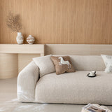 Almond cream chenille sofa cover seen at an angle from the left, styled with printed cushions