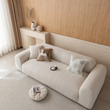 Wide angled view of the almond cream chenille sofa cover on a rounded sofa with a floor pouf