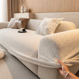 Hand pulling the elastic hem of the almond cream chenille cover around the armrest