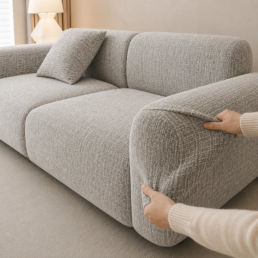Two hands fitting the stone mist chenille cover over the rounded armrest, showing stretch fit