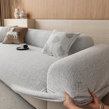 Hands tucking the stone mist chenille cover under the rounded armrest for a snug fit