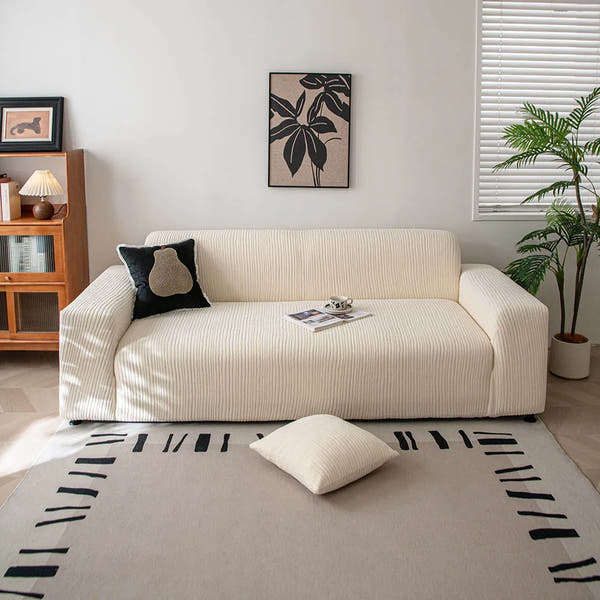 Cream whisper corduroy stretch sofa cover in a bright living room with framed art and plant