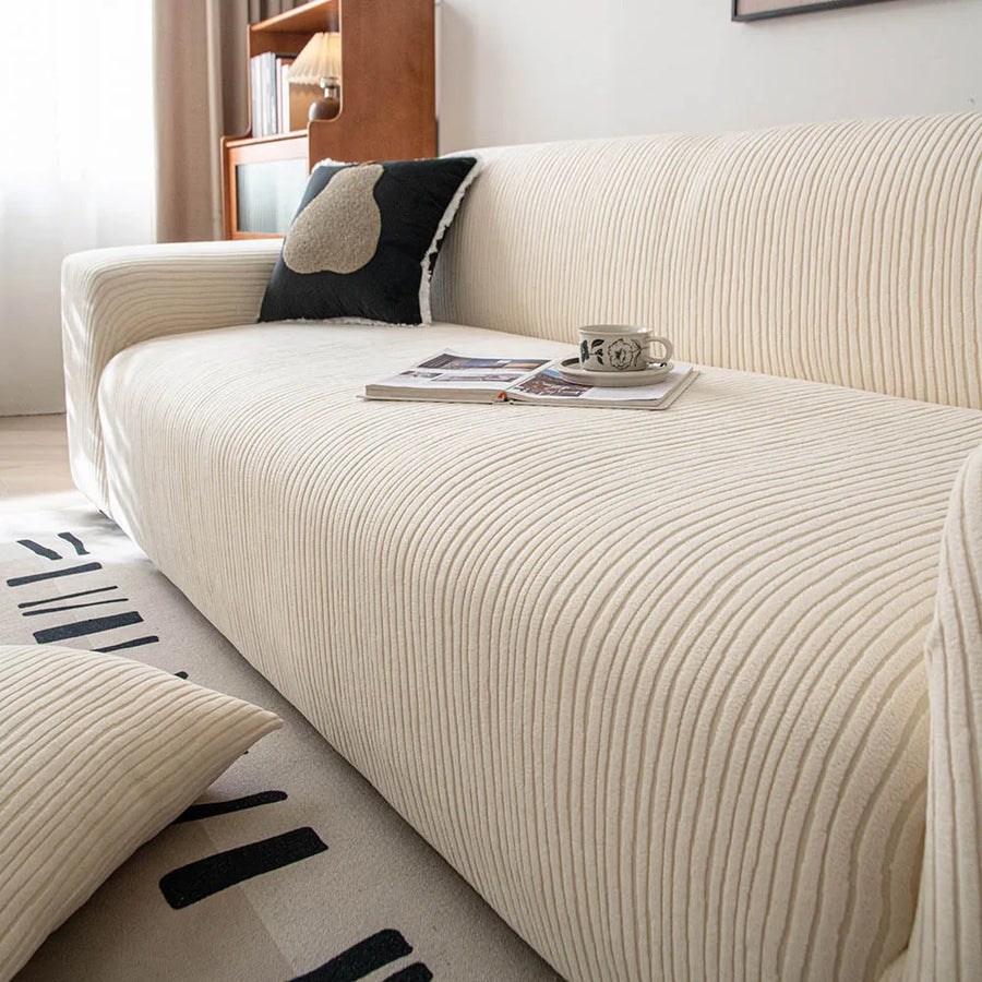 Angled view of cream whisper corduroy sofa cover with an open book and cup on the seat