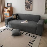 Angled view of graphite shadow corduroy sofa cover with a black cushion and coffee cup