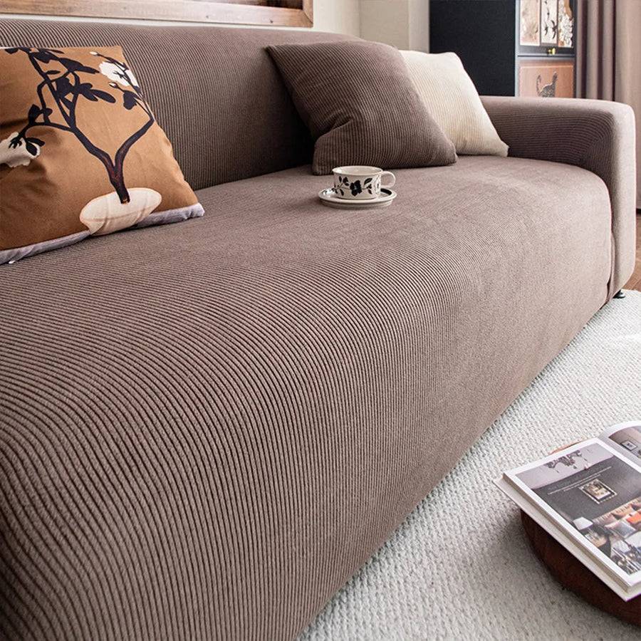 Angled view of mocha brown corduroy sofa cover with cushions and coffee cup on the seat