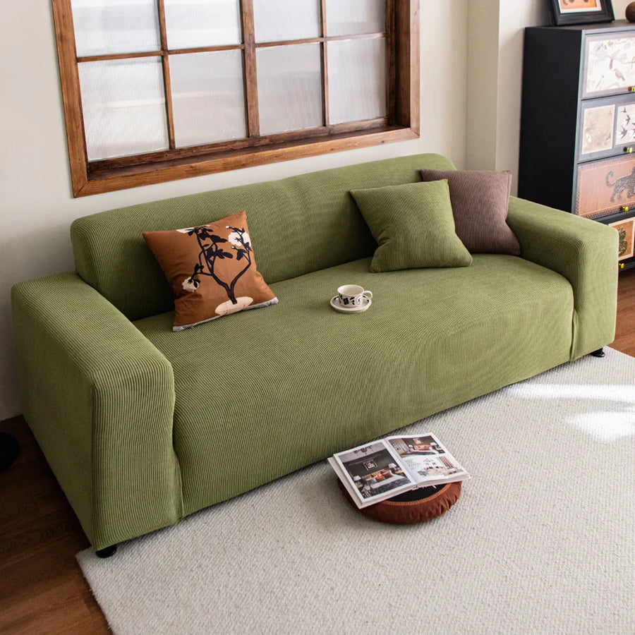 Olive green corduroy sofa cover in a warm living room with layered cushions and rug