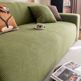 Angled detail of olive green corduroy sofa cover with a cushion and coffee cup