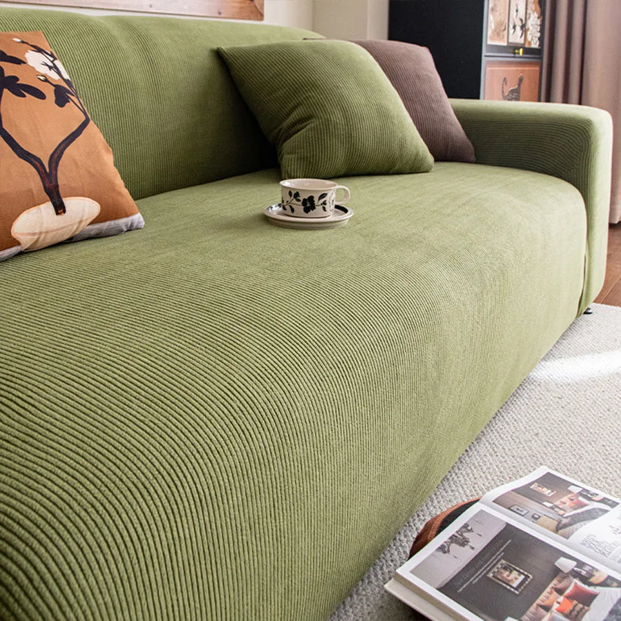 Angled detail of olive green corduroy sofa cover with a cushion and coffee cup