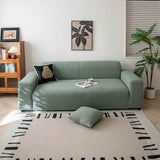 Olive mist corduroy stretch sofa cover in a bright living room with framed art and plant