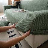 Hands stretching the olive mist corduroy cover snugly over a sofa seat cushion
