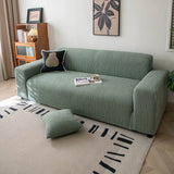Olive mist corduroy sofa cover styled in a sunlit room with a patterned rug and cushion