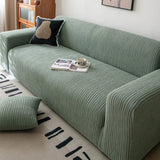 Angled view of olive mist corduroy sofa cover with a matching floor cushion in a cozy lounge