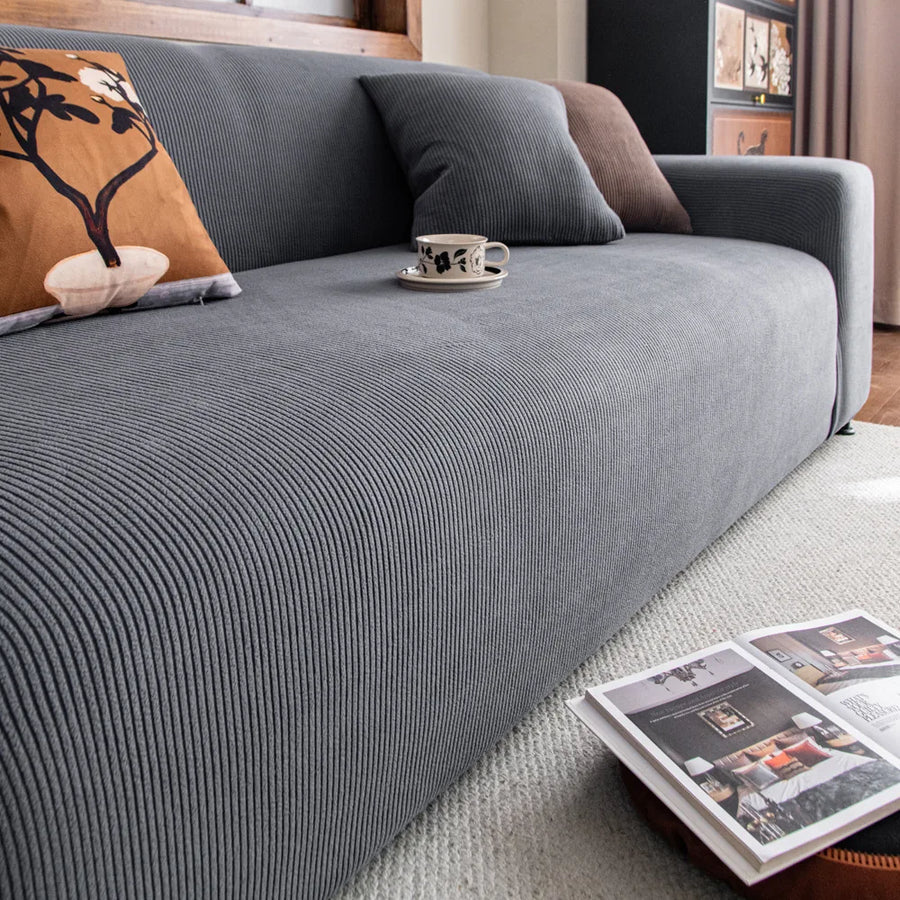 Angled view of the Steel Gray corduroy sofa cover styled with cushions and a coffee cup