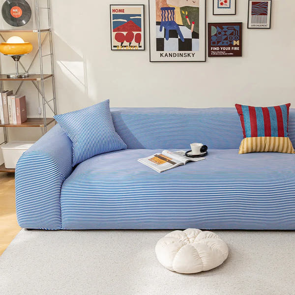 Blue striped ice silk sofa cover in a bright room with a gallery wall, an open magazine and a coffee cup