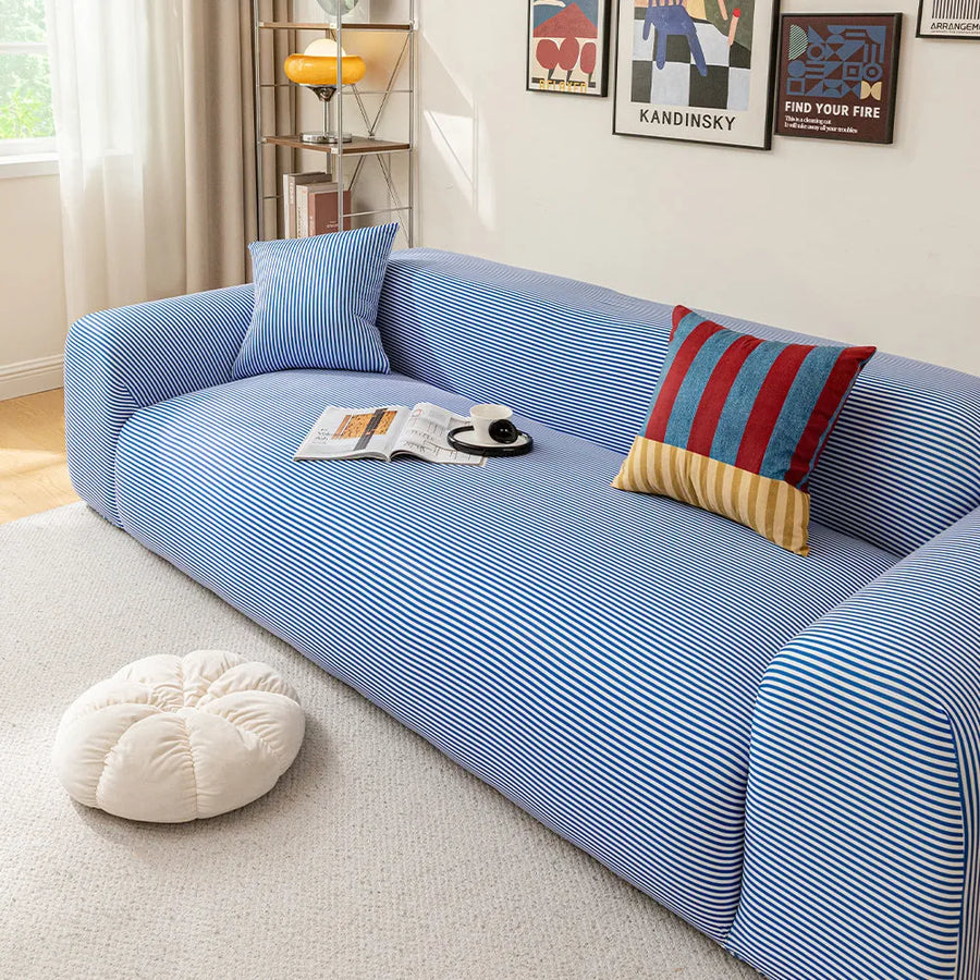 Angled view of the blue striped ice silk sofa cover, smooth stripes styled with an open magazine and coffee