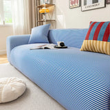 Corner view of the blue striped ice silk sofa cover with cushions and a floor pouf in a sunlit room