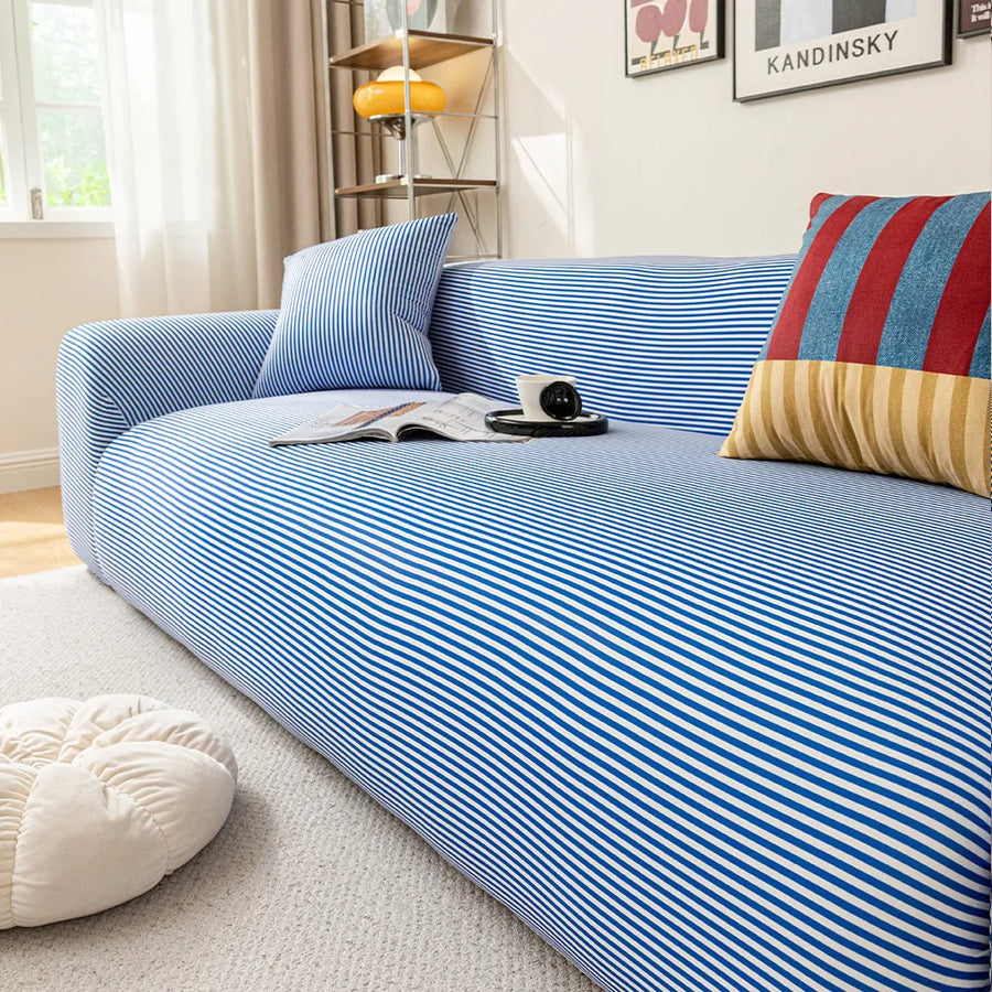 Corner view of the blue striped ice silk sofa cover with cushions and a floor pouf in a sunlit room
