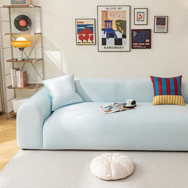 Light blue striped ice silk sofa cover in a bright room with a gallery wall, magazines and a coffee cup