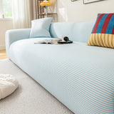 Angled view of the light blue striped ice silk sofa cover, smooth stripes styled with magazines and coffee