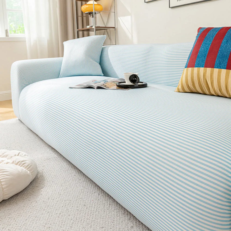 Angled view of the light blue striped ice silk sofa cover, smooth stripes styled with magazines and coffee