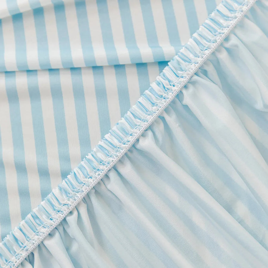 Close-up of the stretchy ruffled elastic hem trimming the underside of the light blue striped ice silk cover