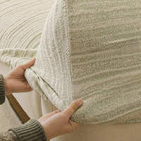 Hands fitting the cream ivory jacquard cover over a sofa seat, showing its stretchy textured weave