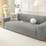 Angled view of the mist grey jacquard sofa cover, wavy texture styled with a teacup and cushions