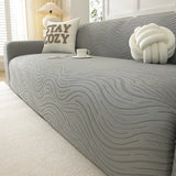 Mist grey jacquard sofa cover in a sunlit room with a table lamp, cozy cushion and teacup
