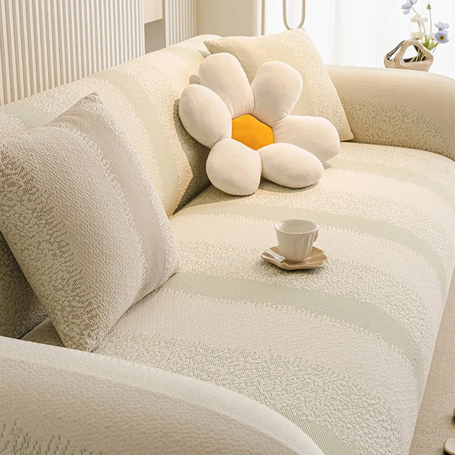 Corner view of the cream sage striped jacquard cover fitted on an L-shaped sofa with a flower cushion