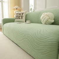 Angled view of the sage green jacquard sofa cover, wavy texture styled with a teacup and cushions