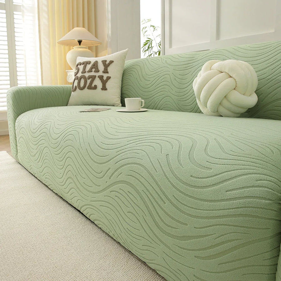 Angled view of the sage green jacquard sofa cover, wavy texture styled with a teacup and cushions