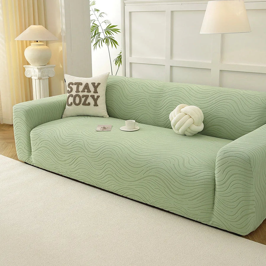 Sage green jacquard sofa cover in a sunlit room with a table lamp, plant and decorative cushions