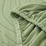 Close-up of the stretchy elasticated hem tucking the sage green jacquard cover under the sofa