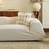 Hand stretching the sand linen jacquard cover over a sofa armrest, with a faux fur cushion and flowers behind