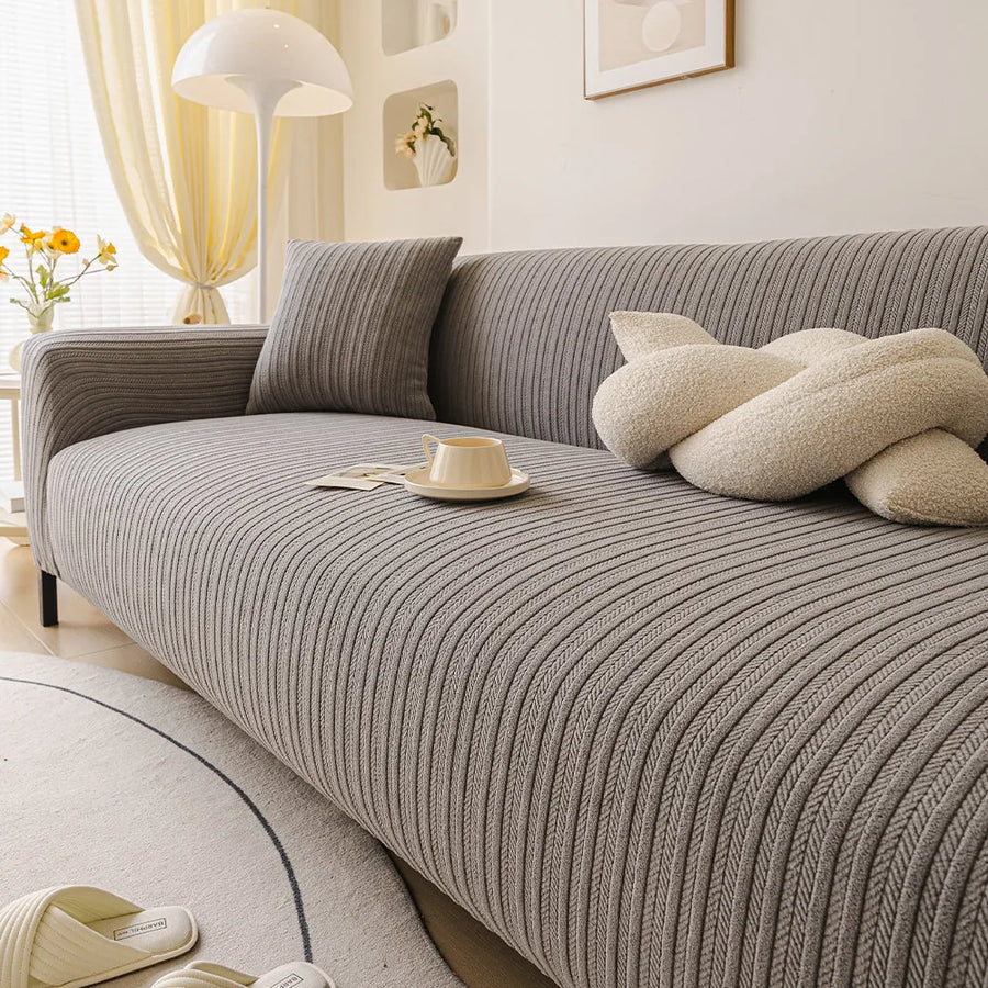 Angled seat view of the charcoal ribbed knit cover with a knot cushion, cup and floor lamp.