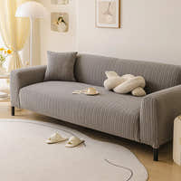 Charcoal ribbed knit sofa cover in a bright living room, angled view with a knot cushion and coffee cup.