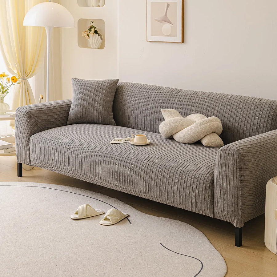 Charcoal ribbed knit sofa cover in a bright living room, angled view with a knot cushion and coffee cup.