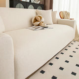 Close-up of cream linen knit sofa cover seat with decorative cushions and open magazine