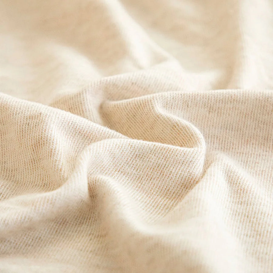 Macro of cream linen knit fabric showing fine twill weave and natural flecks