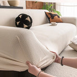 Hands stretching the ivory sand knit cover over a sofa armrest to show its elasticity