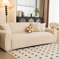 Sofa dressed in sand beige knit cover in a living room, angled view with a ball cushion and coffee cup.