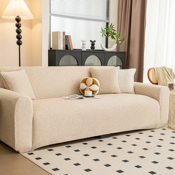 Sofa dressed in sand beige knit cover in a living room, angled view with a ball cushion and coffee cup.