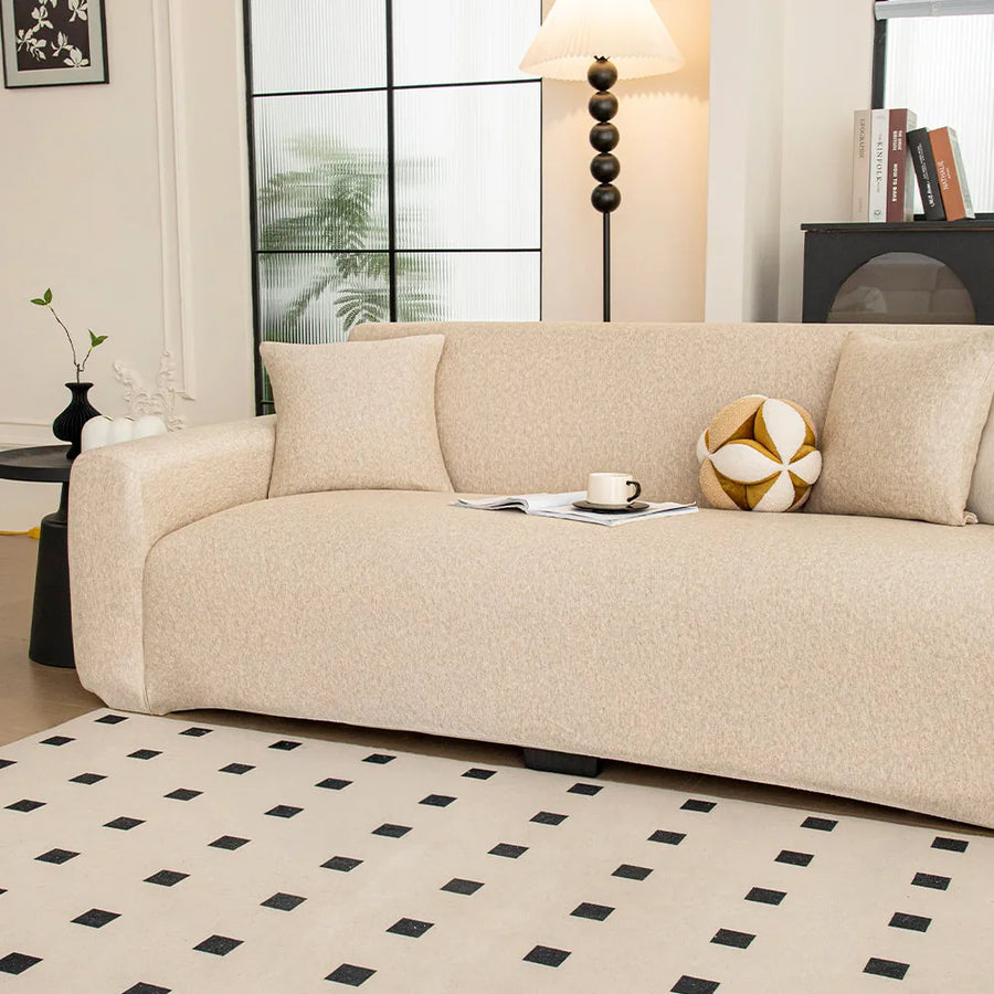 Angled view of the sand beige knit seat and armrest styled with a cushion and cup by a window.