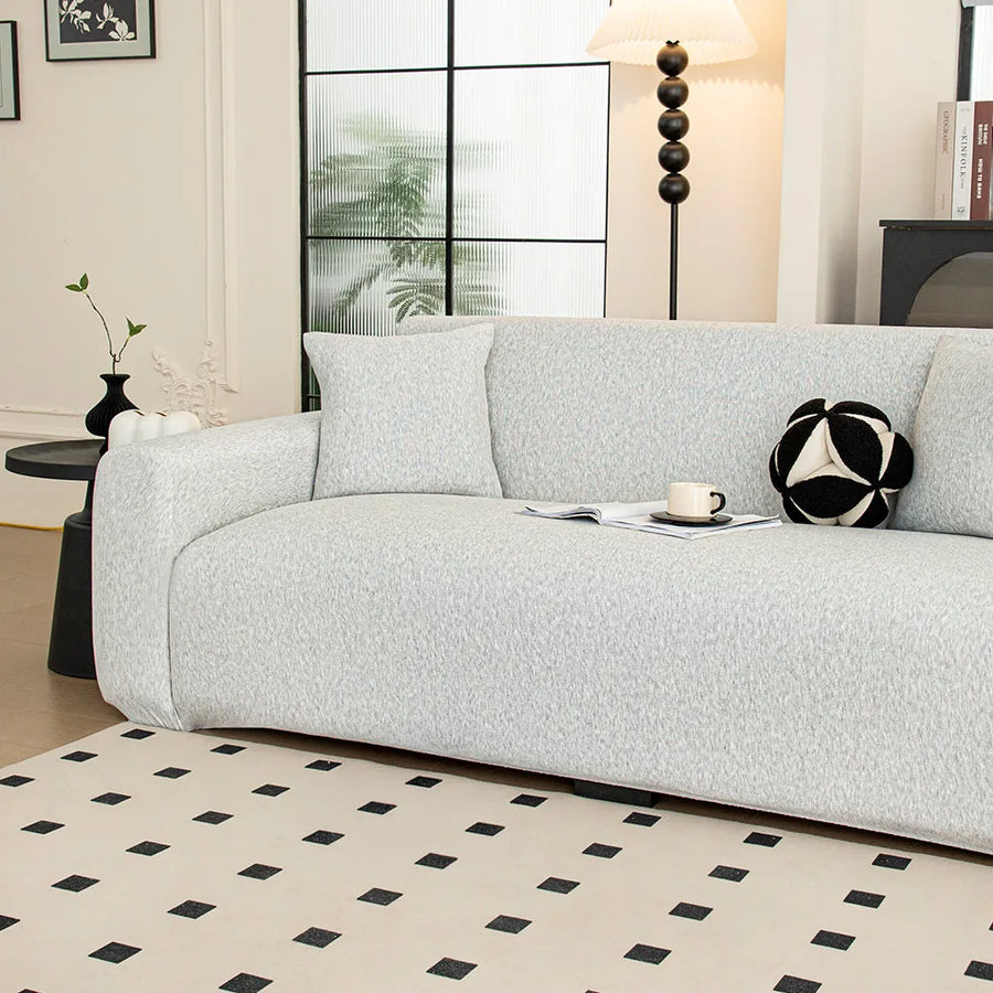 Angled view of silver grey knit sofa cover in a sunlit room with black and white cushion