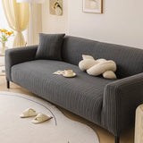 Slate charcoal ribbed knit sofa cover in a sunlit living room, angled seat view with a knot cushion.